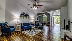 A spacious living room with hardwood floors, a ceiling fan, and a large window.