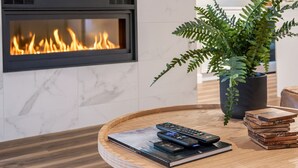 Una sala de estar moderna con chimenea, una mesa de centro redonda de madera, un helecho en maceta y una pila de libros.