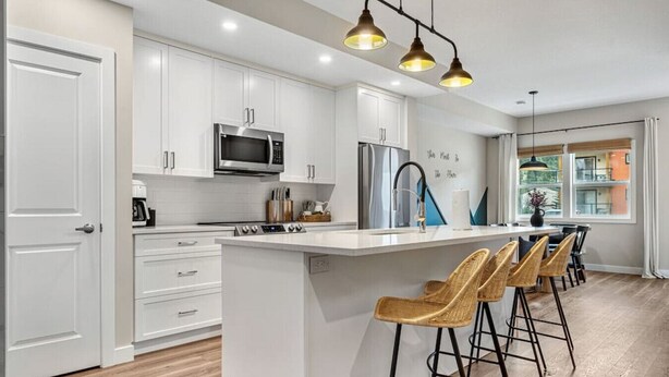 Una cocina moderna con armarios blancos, electrodomésticos de acero inoxidable y una isla central con taburetes de bar.