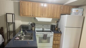 A compact kitchen with wooden cabinets, a white stove, a sink, and a refrigerator.