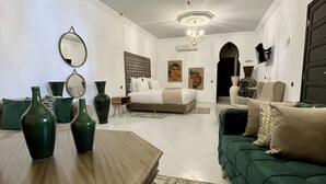A spacious living room with a large sofa, a wooden coffee table, and two green vases. There is a chandelier hanging from the ceiling and a large mirror on the wall.