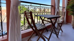 A balcony with a table and chairs, a potted plant, and a view of the sky and greenery.