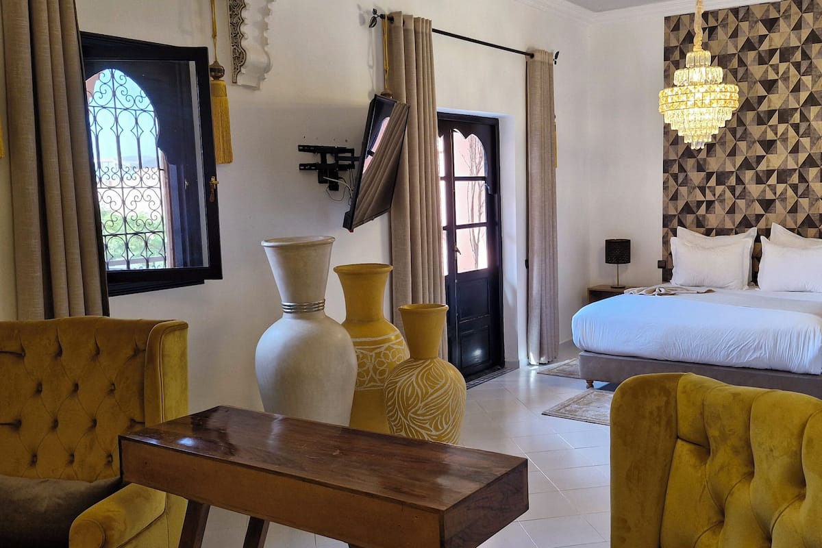A hotel room with a bed, two chairs, a small table, and decorative vases.