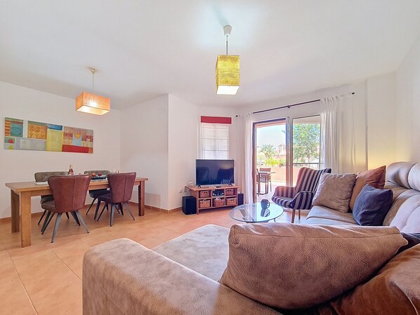 A living room with a sofa, a coffee table, a TV, and a dining area with chairs and a table.