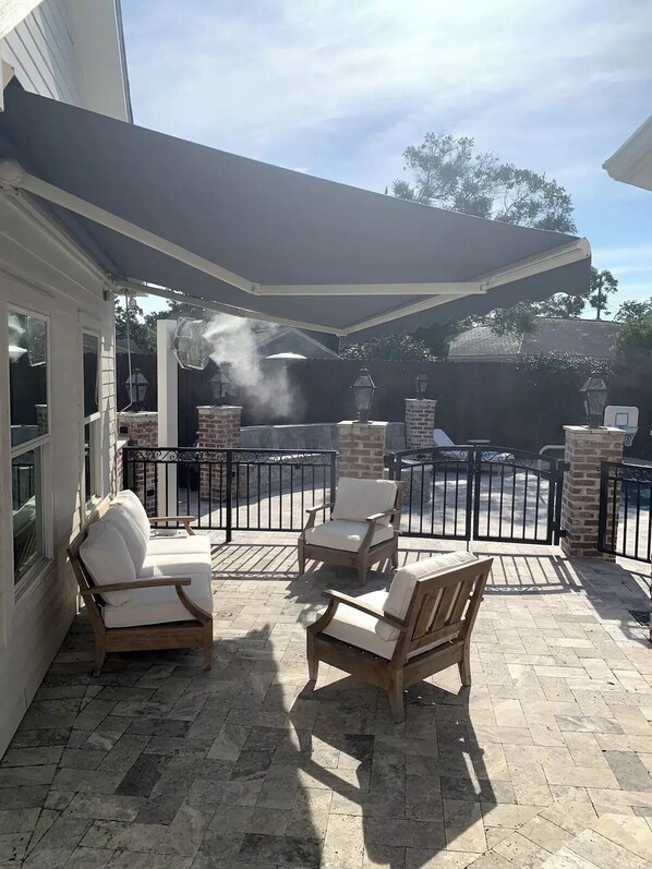 Relax in the comfort of this patio, featuring a brick floor, cushioned chairs, and a wooden table, all shaded by a large umbrella.