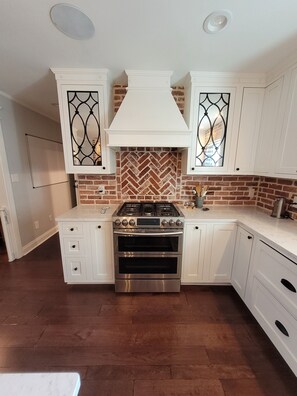 Kitchen features a central gas stove, double oven, and herringbone-patterned brick backsplash.