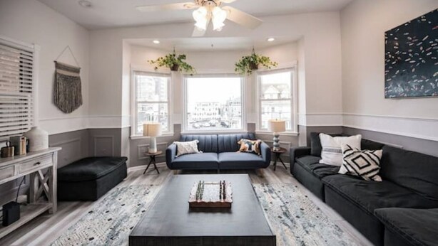 Ein modernes Wohnzimmer mit einer dunkelgrauen Sofagarnitur, einem Couchtisch und Blick auf die Stadt durch große Fenster.