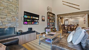 A modern living room with a stone wall, a flat-screen TV displaying movies, a bookshelf, and a cozy seating area with a leather couch and a coffee table.