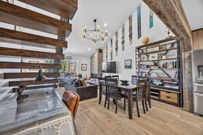 Un salon moderne comprenant un coin repas, des poutres en bois, un mur en pierre et une bibliothèque.
