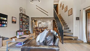 A spacious living area with a leather sofa, a coffee table, and a bookshelf. A staircase with wooden steps leads to an upper floor.