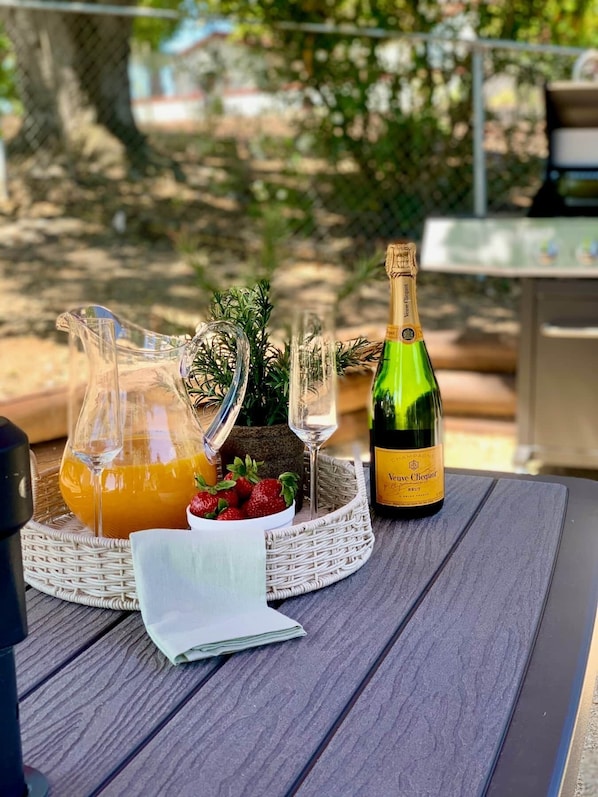 A table set with a bottle of champagne, a pitcher of orange juice, a glass, and a basket with strawberries and greenery.