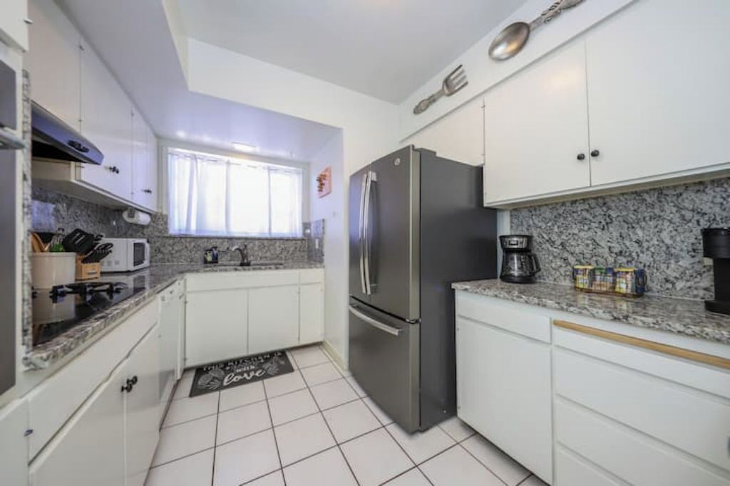 A modern kitchen with white cabinets, a stainless steel refrigerator, a microwave, and a coffee maker.