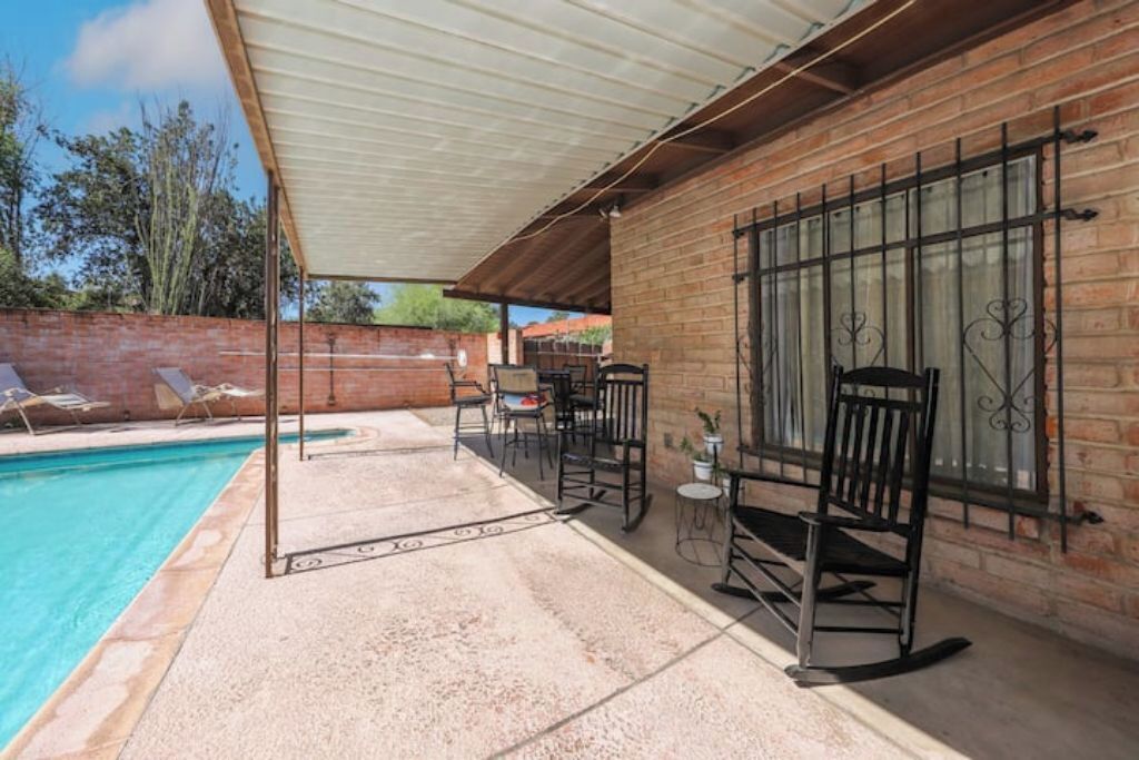 A covered outdoor area with a pool, lounge chairs, and a brick wall.