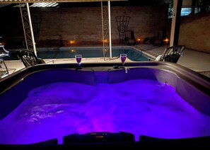Ett bubbelbad med två glas vin, omgivet av stolar och en tegelvägg i bakgrunden.