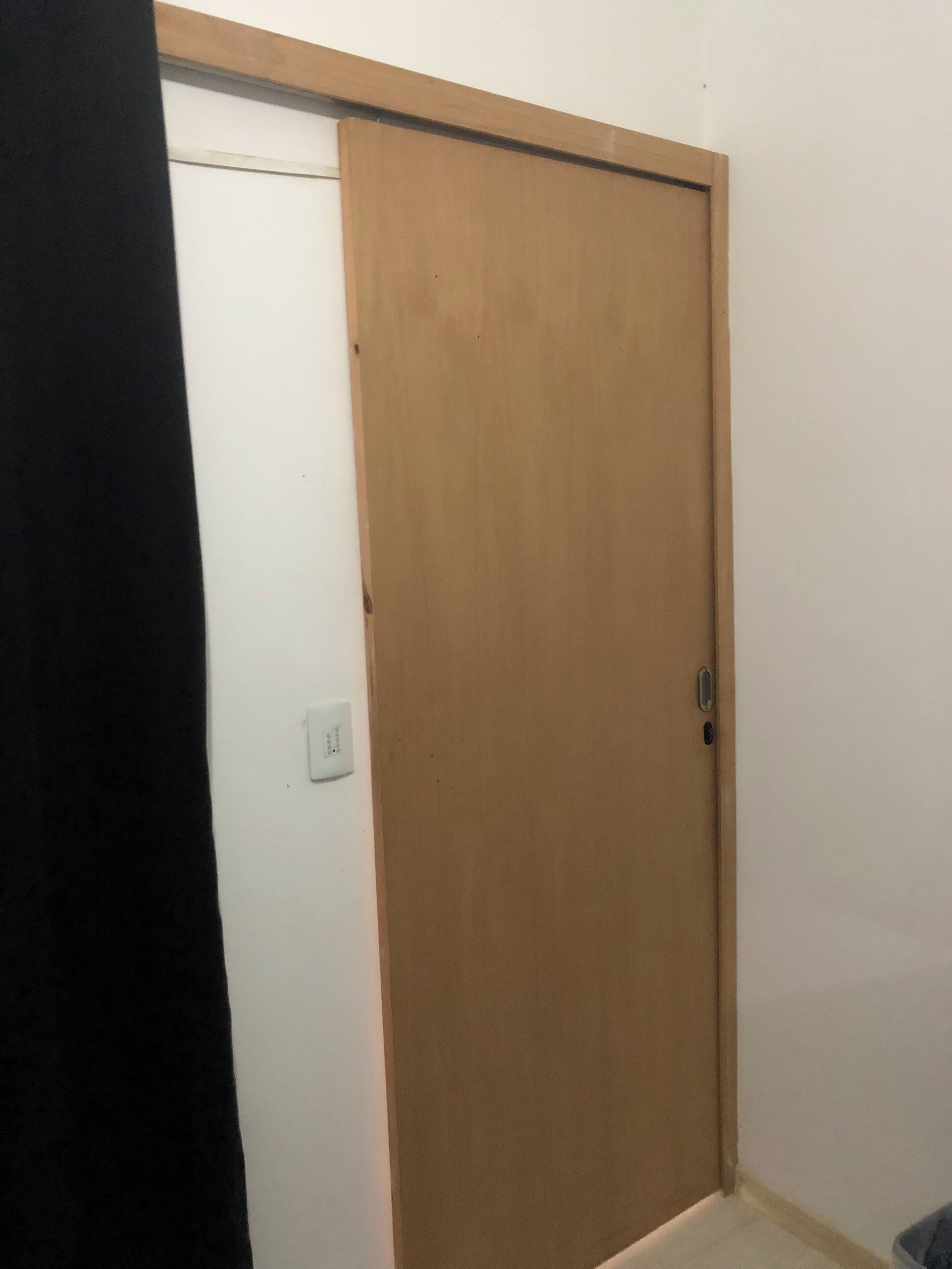 A closed wooden door with a sliding mechanism, a white wall, and a light switch visible on the wall.