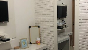 A room with a white brick wall, a desk with a computer, a mirror, and a television on the wall. - Single Room Centro Avaré  (Braz II Avaré)