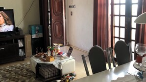 A living room with a television, a dining table with chairs, a patterned rug, and a dog on the rug. - Single Room Centro Avaré  (Braz II Avaré)
