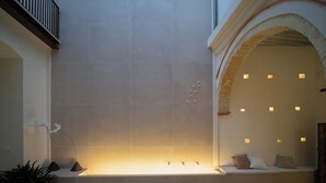 A modern interior with a central illuminated wall, a seating area with cushions, and a balcony with a railing. - Deluxe apartment (Sanlúcar de Barrameda)