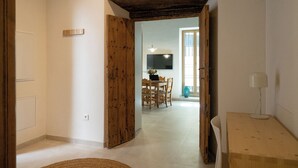 A room with a wooden door, a dining area with a table and chairs, and a TV mounted on the wall. - Deluxe apartment (Sanlúcar de Barrameda)