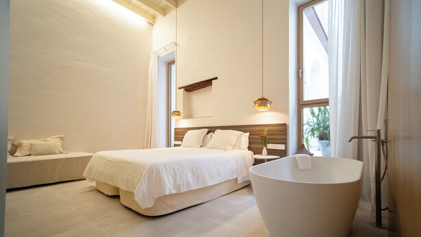 A modern bedroom with a large bed, a bedside table, a built-in bench, and a freestanding bathtub. - Deluxe apartment (Sanlúcar de Barrameda)