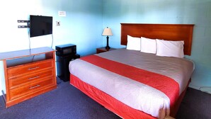 Una habitación de hotel con cama, escritorio con cajones, televisor, lámpara y microondas.