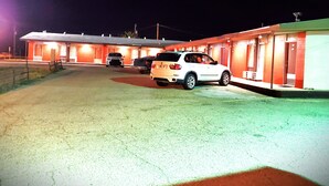 Un motel con tres habitaciones, cada una con una puerta y una ventana. Hay dos coches aparcados delante del motel.