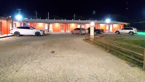 Un motel con una fila de habitaciones, un camino de grava y coches estacionados al frente.