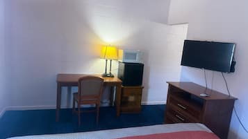 Habitación de hotel con cama, escritorio con silla, televisor, microondas y cómoda.