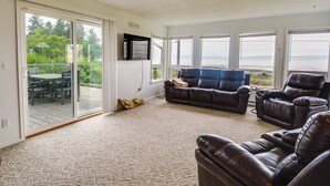 A spacious living room with a large sliding glass door leading to a deck, a leather sofa, and a recliner. - Seiku Vacation Rental w/ Deck & Ocean Views (Seiku)