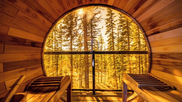 Une pièce circulaire en bois, dotée d’une grande fenêtre, de bancs en bois et d’un escalier menant à la fenêtre.