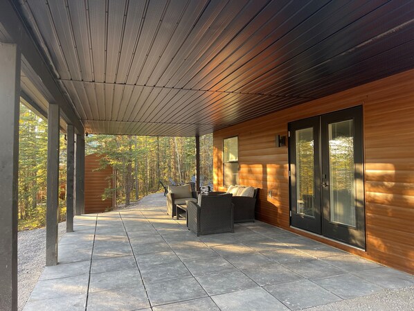 A covered patio area with a stone floor, wooden walls, and large sliding glass doors. - Modern Rustic A-Frame Cabin with Barrel Sauna (Nordegg)