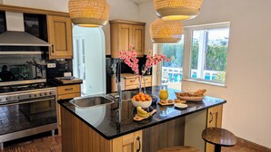 Una cocina moderna con armarios de madera, una isla central con taburetes, una estufa y lámparas colgantes.