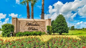 Windsor Palms Schild mit Steinverkleidung, Palmen und einem angelegten Garten mit roten und gelben Blumen.