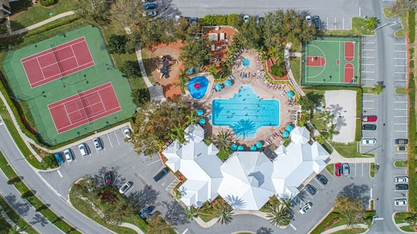 An aerial view of a resort with multiple tennis courts, a large swimming pool, and a parking lot.