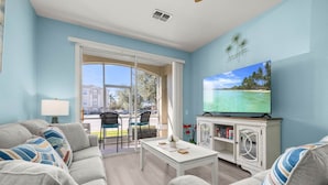 Ein Wohnzimmer mit Sofa, Sesseln, Couchtisch, Fernseher und Blick auf ein Gebäude durch eine Glastür.