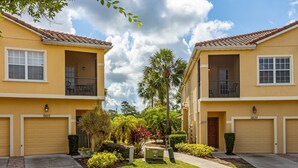 A row of yellow two-story townhouses with balconies, garage doors, and a well-maintained lawn. - Disney Trail-Much loved 2 bedroom Oakwater condo, just 1.5 miles from Disney! (Kissimmee)