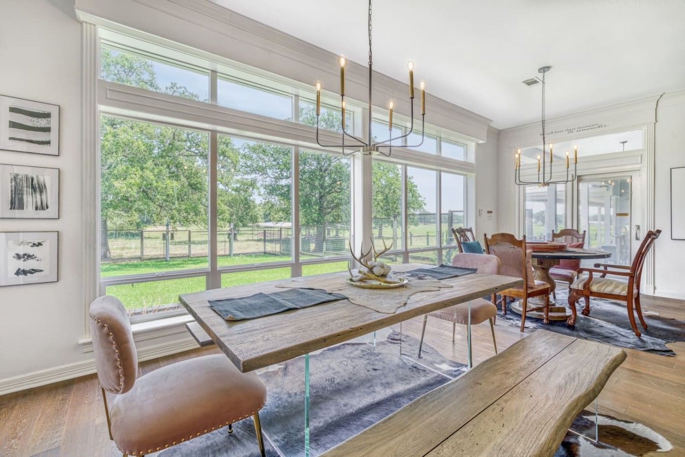 Un comedor con una mesa de madera, sillas y una araña. Amplias ventanas ofrecen vistas al exterior.