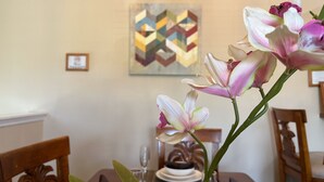 Une table à manger avec des assiettes, un vase rempli de fleurs et un tableau aux motifs géométriques accroché au mur.