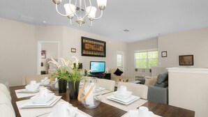 A dining area with a wooden table set for a meal, a television in the background, and a chandelier above. - Lakeside-Beautiful 3 bed Oakwater condo over the lake, just 1.5 miles from WDW! (Kissimmee)