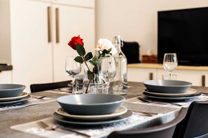 A dining table set with plates, bowls, and glasses, with a bottle and flowers on the table.