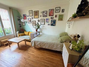 Ein Zimmer mit einem Bett, einem Sofa, einem Tisch und einem Fenster. An der Wand befinden sich gerahmte Bilder.
