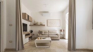 Una sala de estar moderna con un sofá, una mesita de centro y objetos decorativos. Hay un estante de madera con pequeños objetos decorativos y un cuadro en la pared.