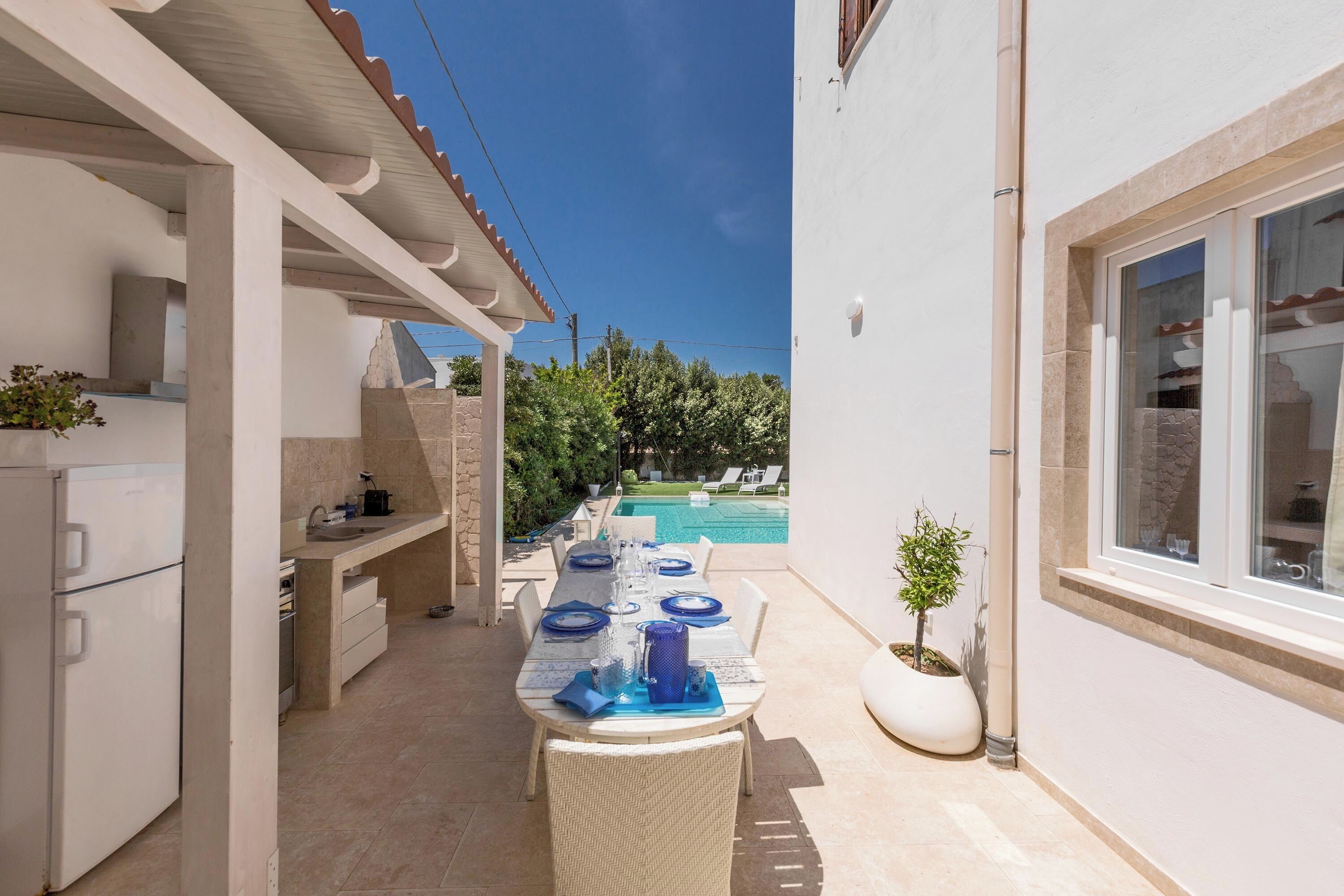 A covered outdoor dining area with a pool in the background.