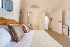 Ein Schlafzimmer mit einem Bett, Kissen, einem Holzkopfende, einem Spiegel, einer Steinwand und einer Tür zu einem anderen Raum.