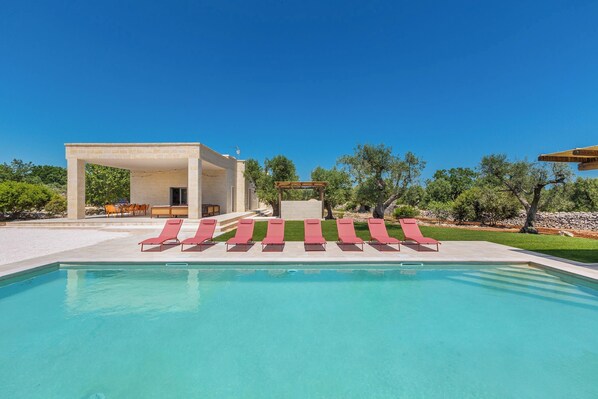 Ein Swimmingpool mit roten Liegestühlen, einer überdachten Sitzgelegenheit und einer Pergola.