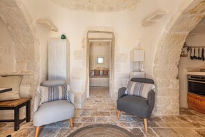 Une pièce aux murs de pierre, avec deux fauteuils, une table en bois et un lit à l’arrière-plan.
