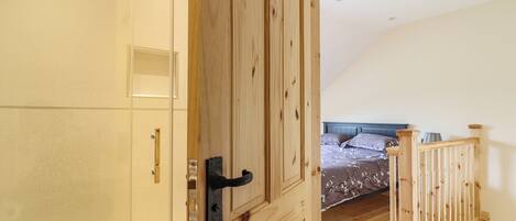 A bedroom with a wooden staircase, a bed with floral bedding, and a wooden door leading to another room.