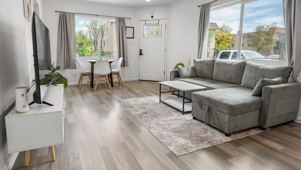 Een moderne woonkamer met een bank, televisie, eettafel, stoelen en een groot raam.