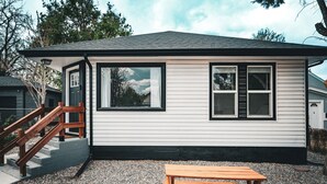 Een gelijkvloers huis met een veranda, een houten trap en een grindpad.