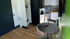 Une cuisine compacte avec des meubles blancs, un lave-linge et un coin repas avec une table recouverte de plastique.